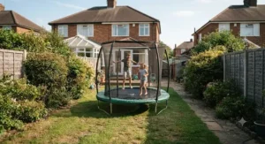 Children bouncing safely on an oval trampoline installed in a long, narrow back garden.