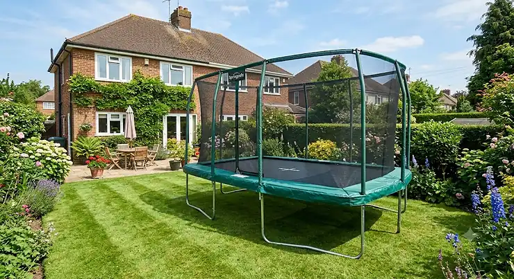 A large garden trampoline set up on a neat lawn in a sunny British backyard.